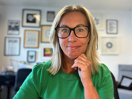 En leende Jessica framför en vägg med tavlor.