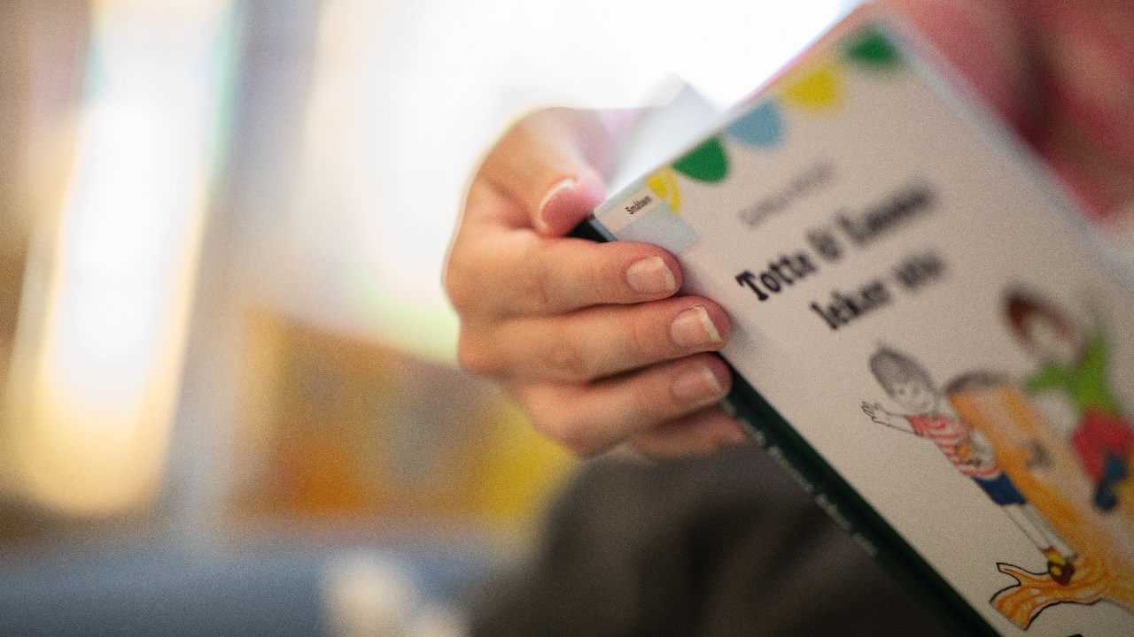 Vuxen hand håller i barnbok vid lässtund