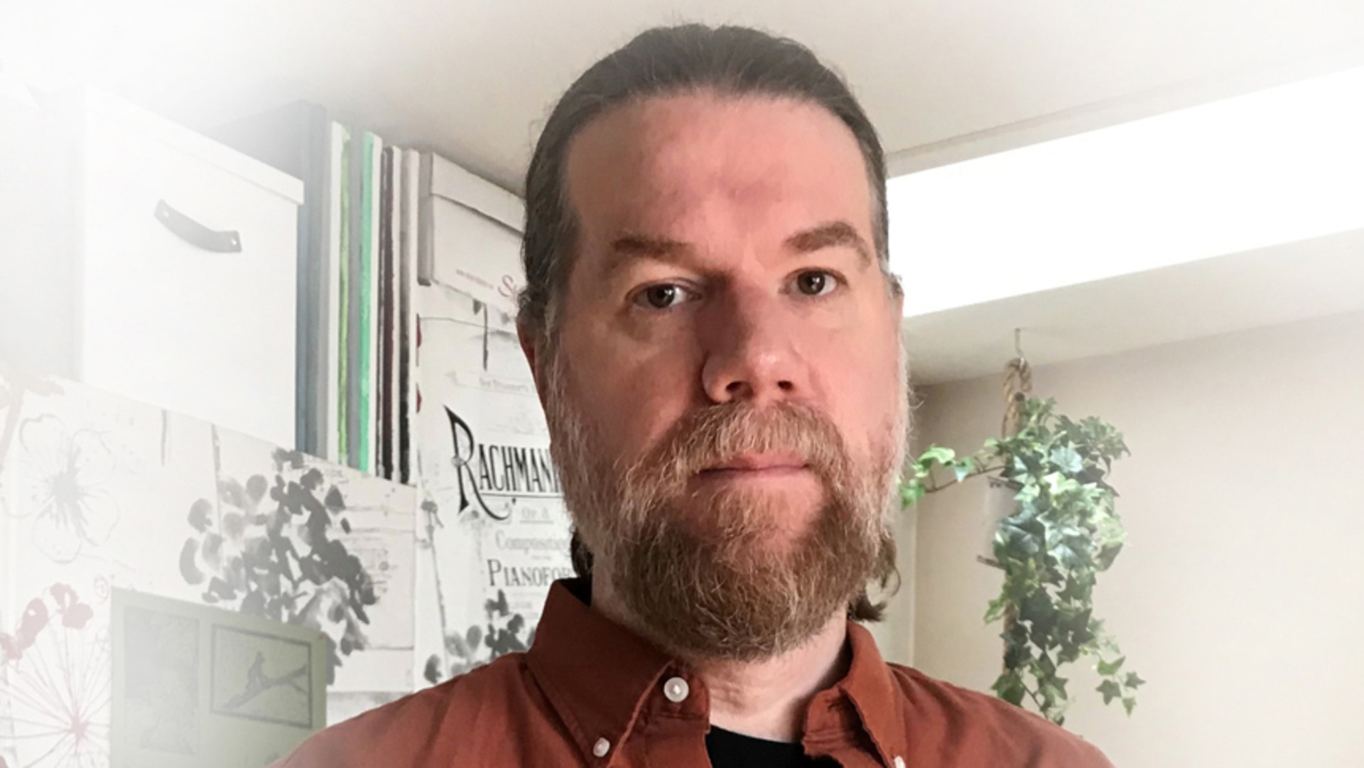 N&auml;rbild p&aring; Thomas Wikberg, med sk&auml;gg och mustasch i brun skjorta framf&ouml;r h&auml;ngande kruklv&auml;xt.