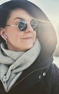 Gill Faulkner med luvjacka tittande upp åt åt sidan bärande runda solglasögon.