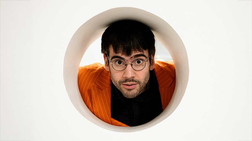 Felix Swahn i orange kavaj tittar ut mot betraktaren genom en rund öppning.