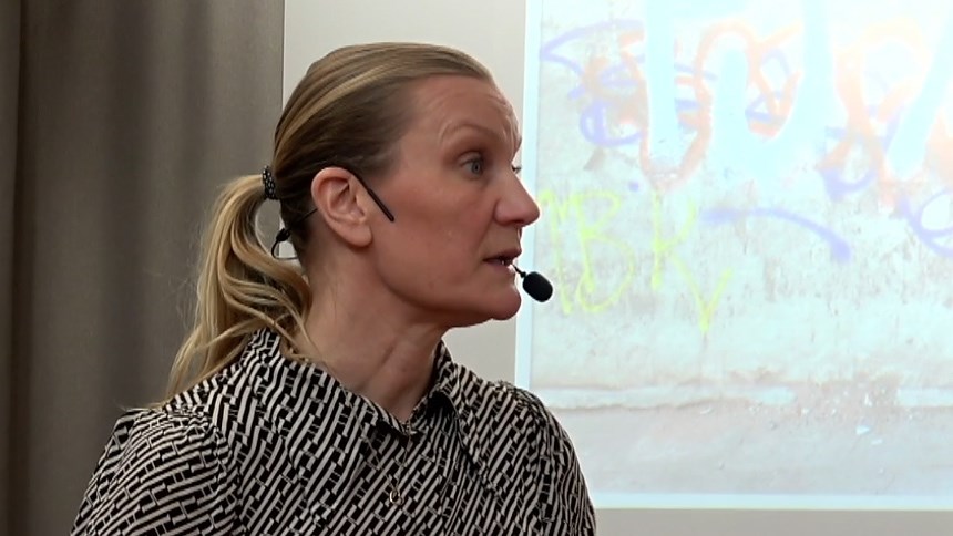 Åsa Konradsson Geuken föreläser på infoteket. På projektorduken bakom visas en målning av hennes bror Mats.