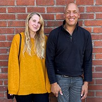 Saga och Niklas Rossi vid en tegelv&auml;gg tittar mot kameran.