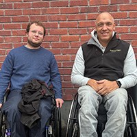 Simon Backhaus Brudzewski och Niklas Rossi i varsin rullstol framf&ouml;r en tegelv&auml;gg-