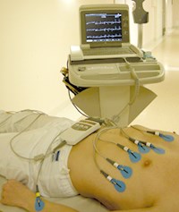 En liggande man med bar överkropp där ett EKG är fastsatt och inkopplat i en datorskärm.