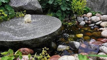 Ett fågelbad med vatten som bubblar upp ur en rundel av granit. 