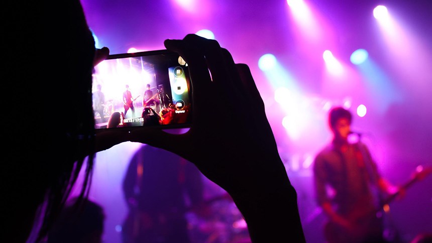 en person håller fotar en konsert med mobilkamera