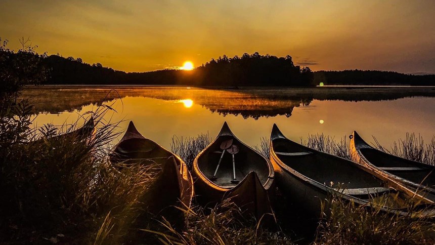 Fem kanoter på strandkant vid en sjö i solnedgång