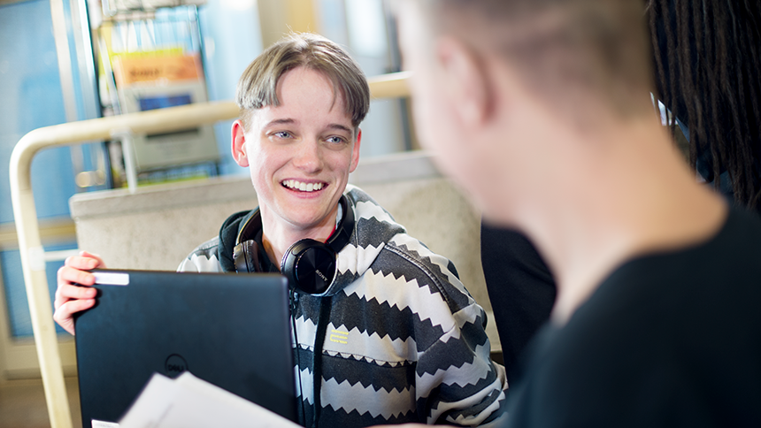 Glad kille med hörlurar runt nacken och laptop i knäet