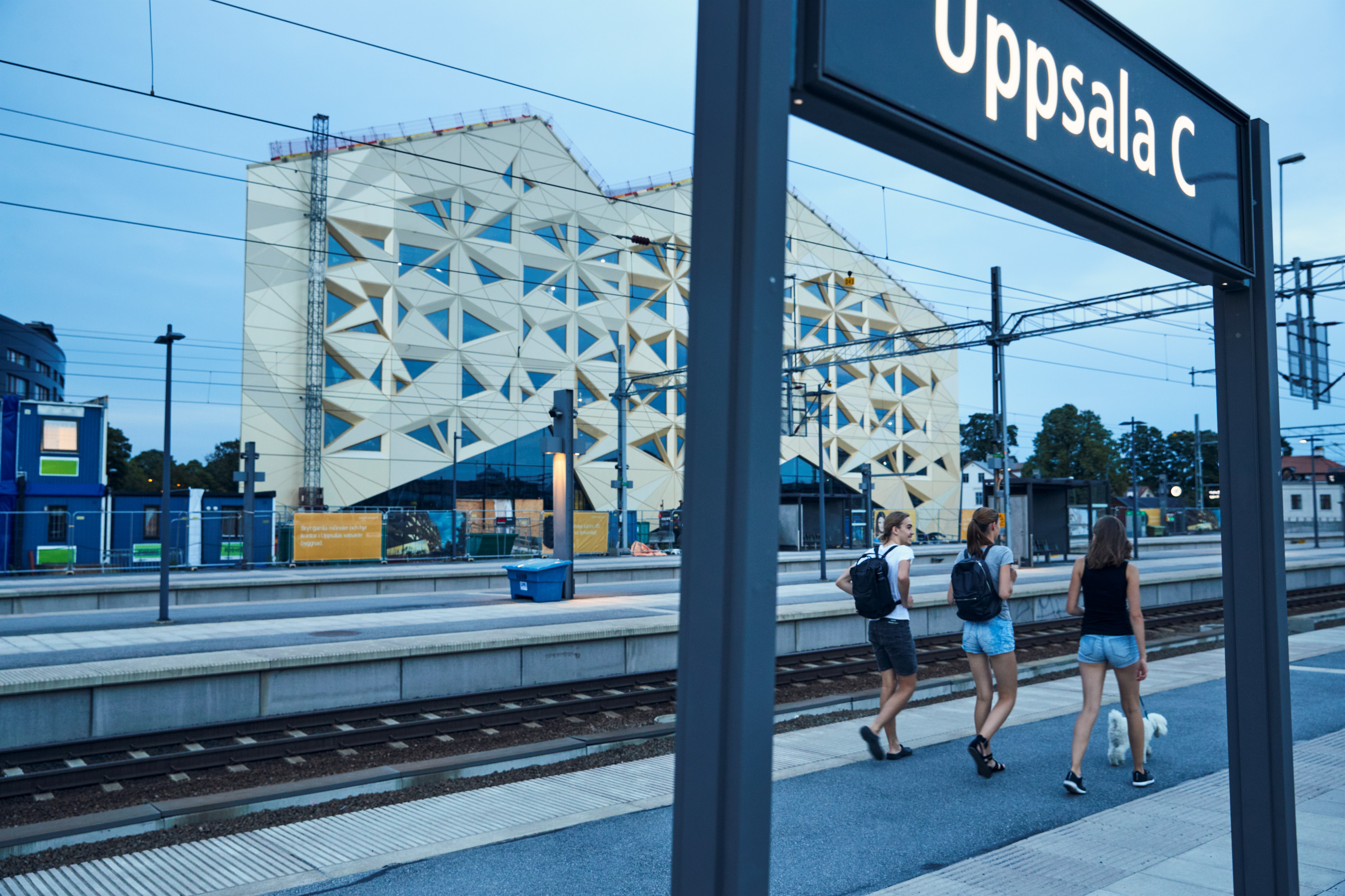 Tre unga personer går på tågperrong i stadsmiljö