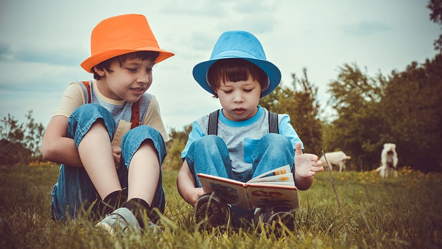 Två barn läser en bok i sommargräs.