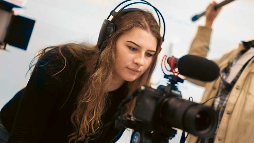 En kvinna sitter bakom en filmkamera med hörlurar