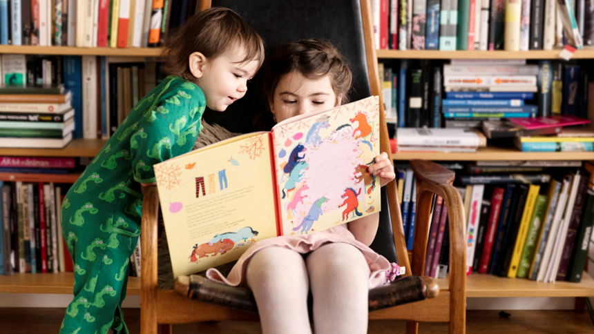 Två barn tittar i bok tillsammans i bibliotek