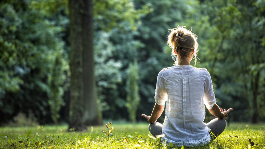 Kvinna sitter på gräset och utövar yoga