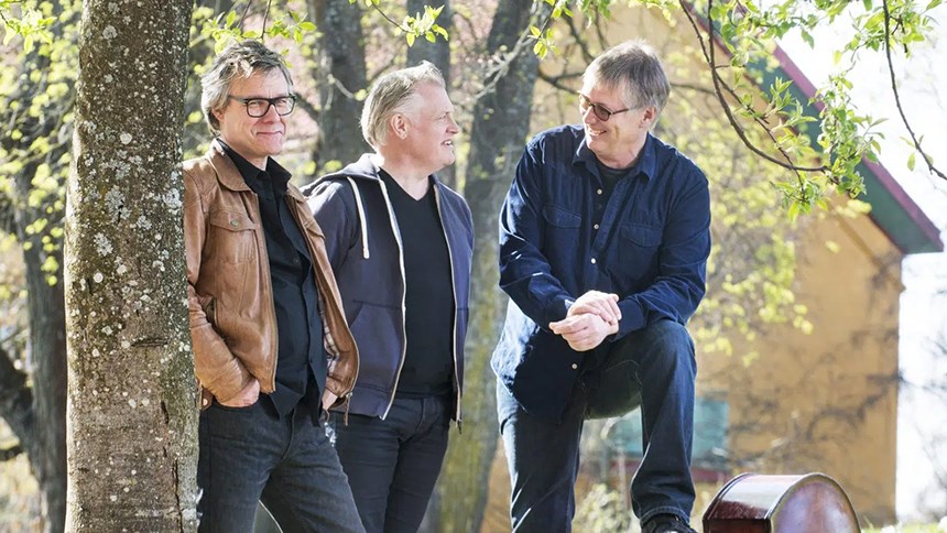 Bandet Trio X, som består av tre medelålders män, poserar utomhus.